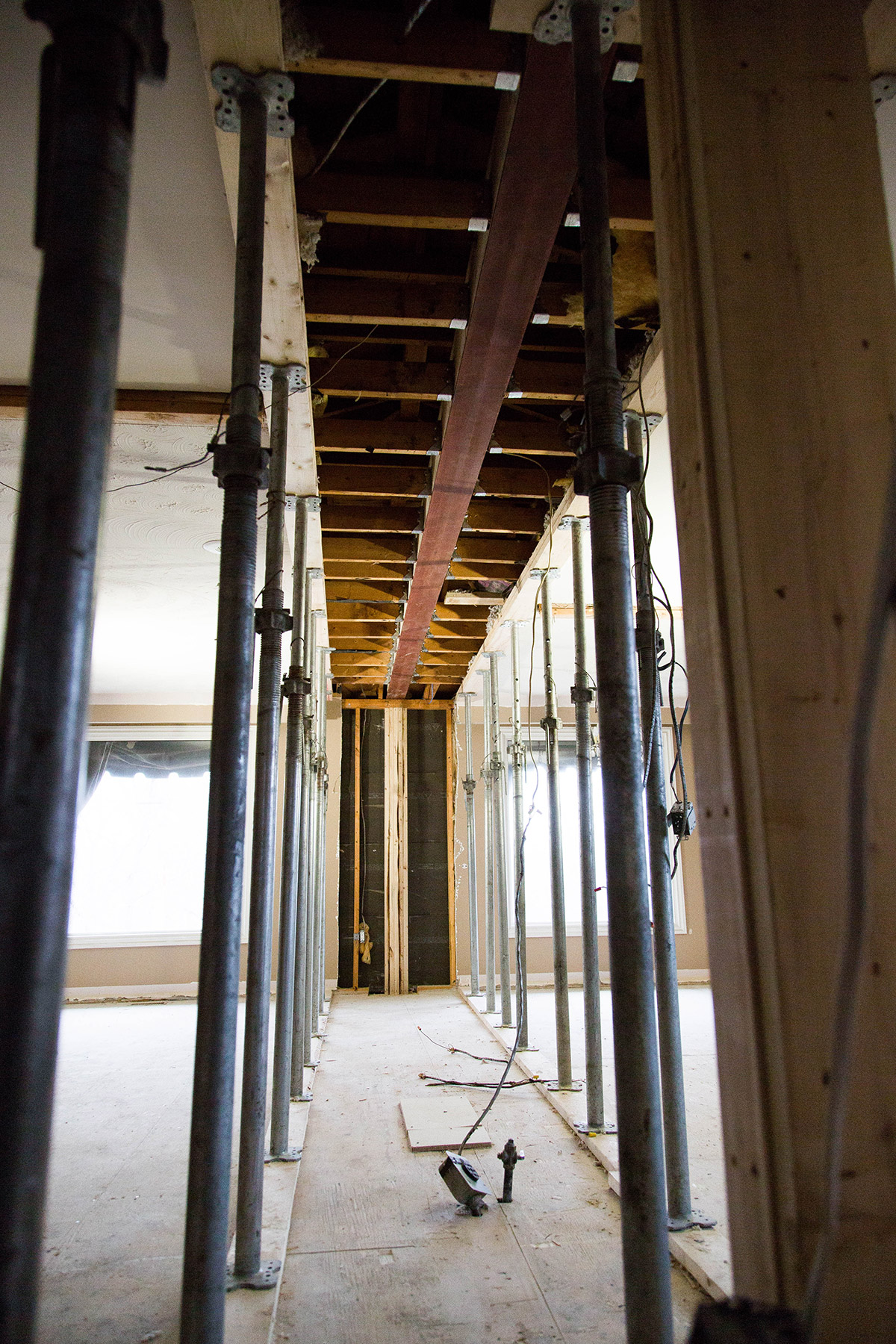 Interior of a building under construction with exposed wooden beams, metal support poles, and unfinished walls.