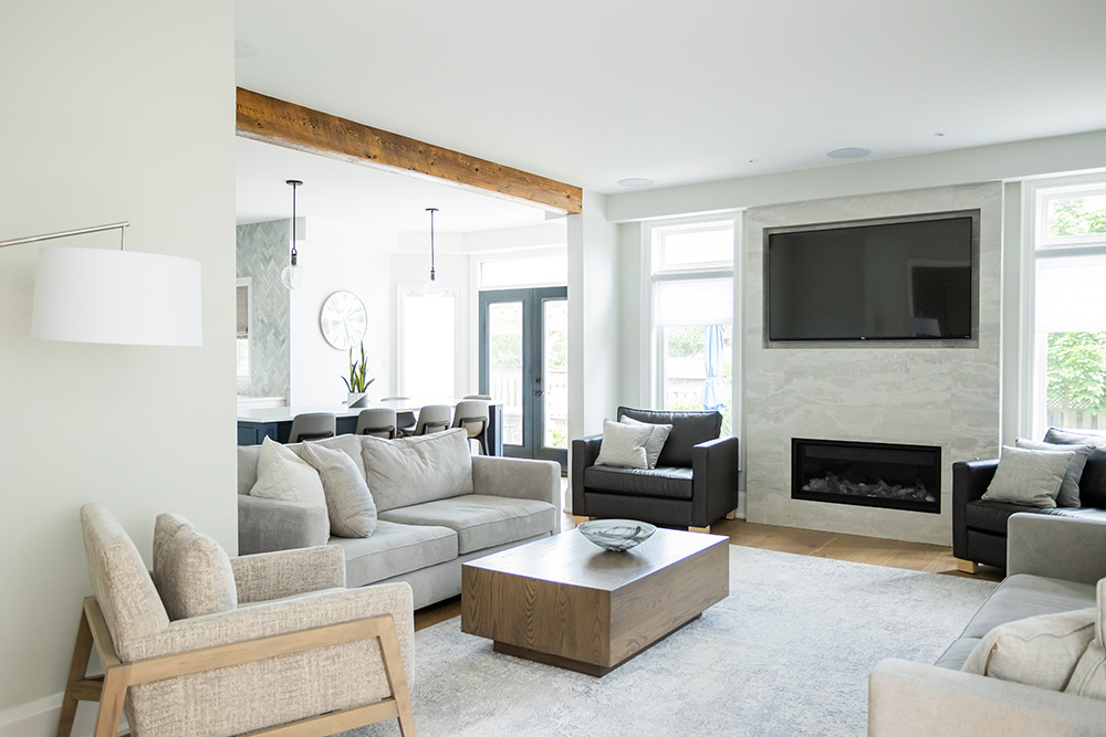 A modern living room with a sectional sofa, armchairs, a fireplace, a mounted TV, and natural light.