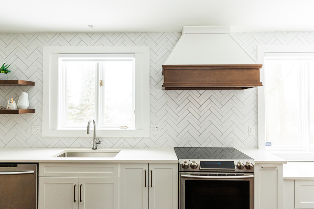 A modern kitchen with white cabinetry, herringbone backsplash, and stainless steel appliances.