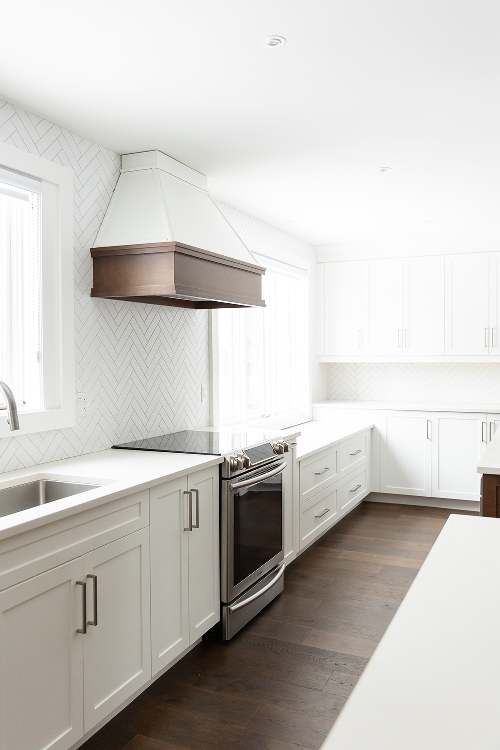 A modern kitchen with white cabinetry, herringbone backsplash, and stainless steel appliances.