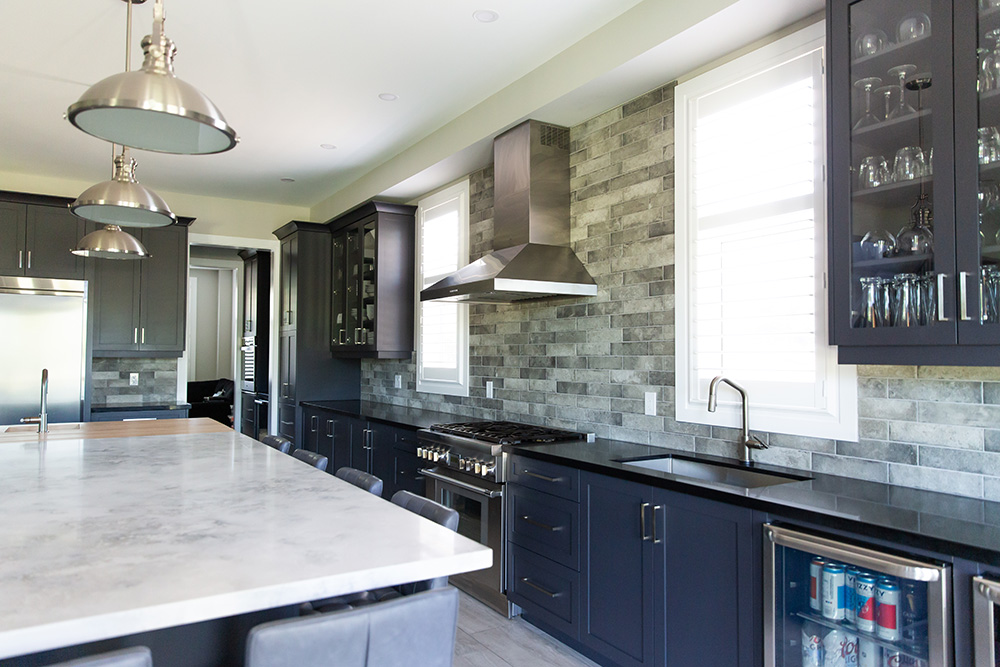 A modern kitchen with dark cabinetry, stainless steel appliances, and a gray stone backsplash.