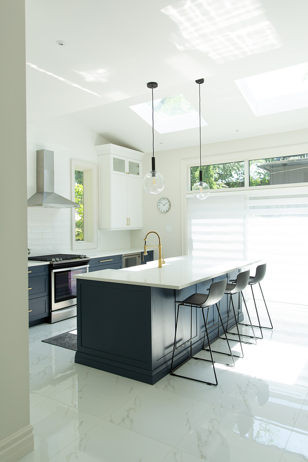 A modern kitchen with white marble floors, white cabinets, a dark island with bar stools, and pendant lights.