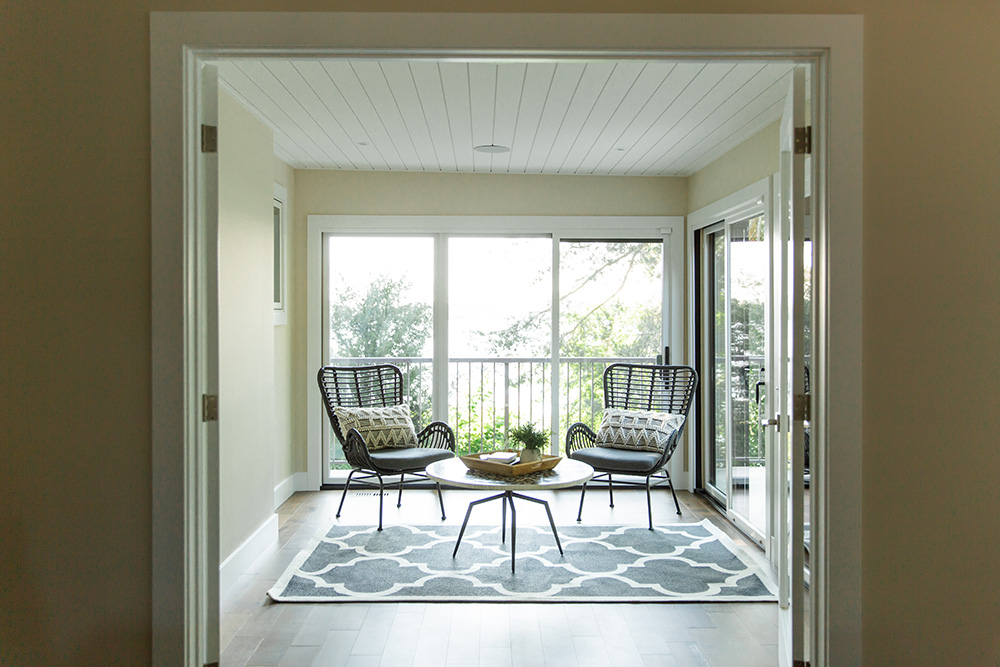 ALT: Double doors open to a cozy sunroom with two chairs surrounded by large windows and glass doors.