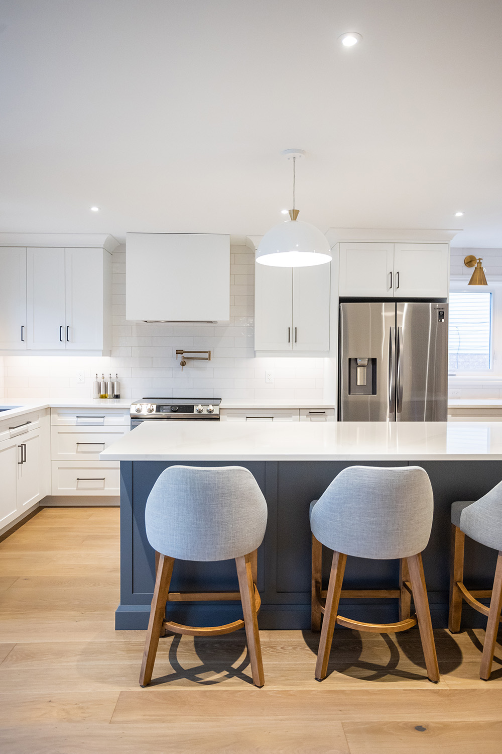 A modern kitchen with white cabinetry, stainless steel appliances, and a breakfast bar with gray stools.