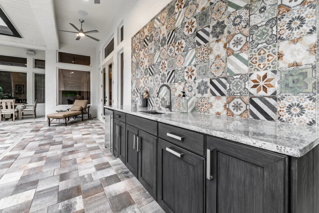 A modern kitchen with patterned backsplash tiles, dark cabinets, and a checkered floor extending to a connected patio area.