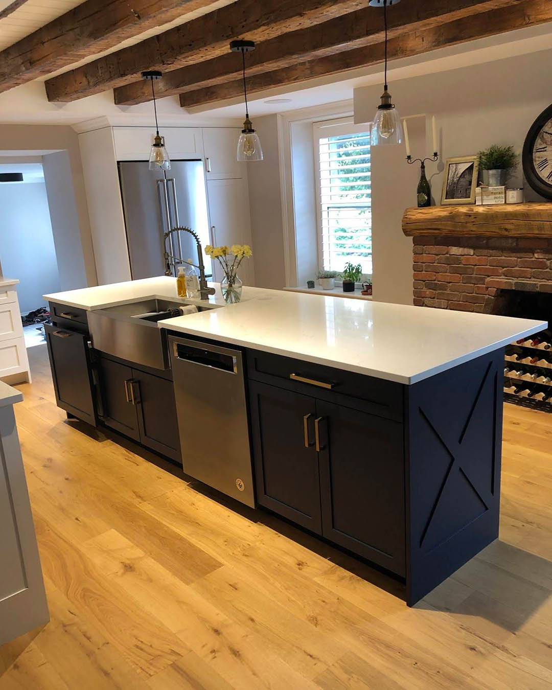 Modern kitchen renovation featuring a central island with dark cabinetry, stainless steel appliances, and a white countertop, complemented by rustic wooden beams and a warm wooden floor, showcasing Heartwood Renovations' craftsmanship.