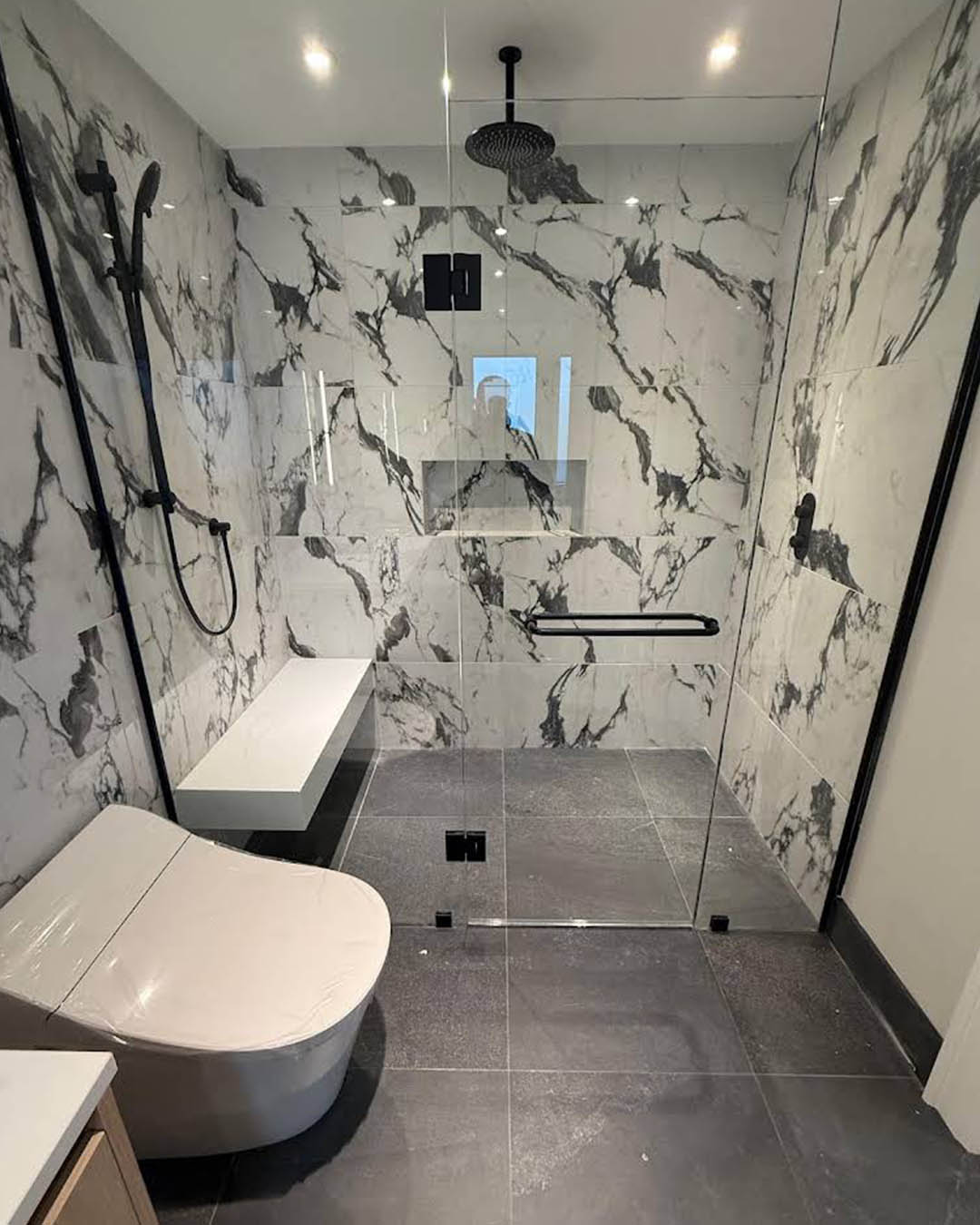 Modern bathroom renovation featuring marble walls, glass shower enclosure, sleek toilet design, and contemporary fixtures, showcasing Heartwood Renovations' craftsmanship in home updates.